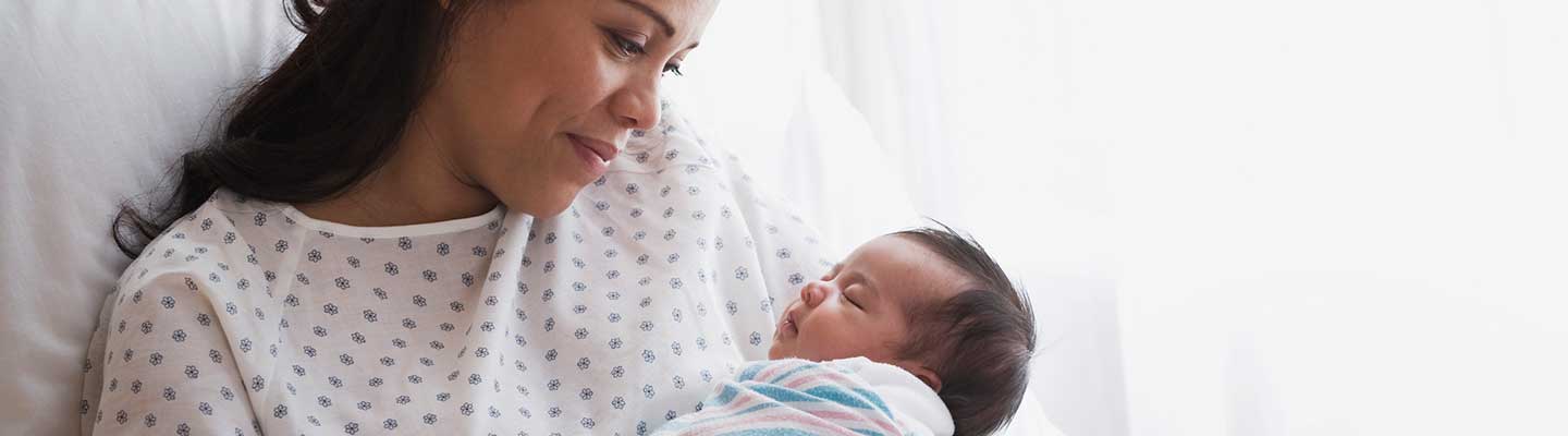 Mom smiling at her newborn wrapped in a blanket