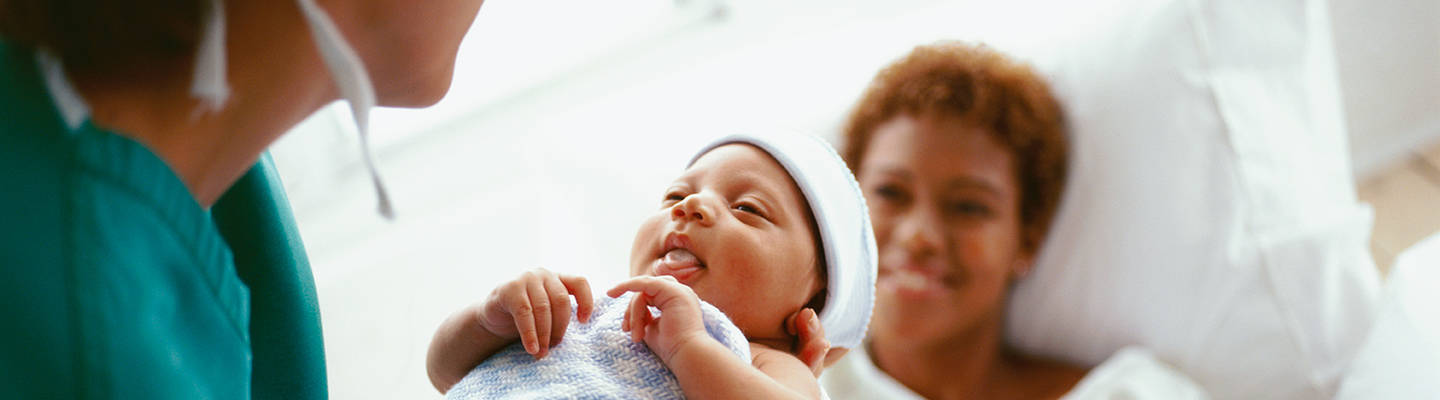 A health provider holds a patient's baby at the mother's bedside.